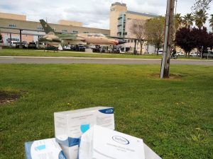 Image of packages of masks in foreground with VA hospital in background. There is also an airplane by the building.