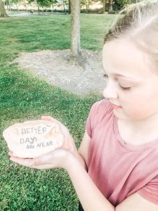 Child holding rock with words "better times are near" painted on it.