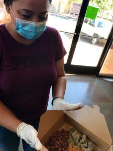 Image of woman holding a boxed meal with rice, beans and chili verde inside.