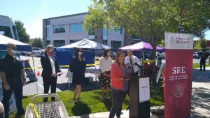 Image of woman standing at podium with people standing behind her at a distance.