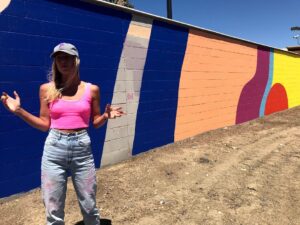 Image of woman standing in front of painted walls hands outstretched.