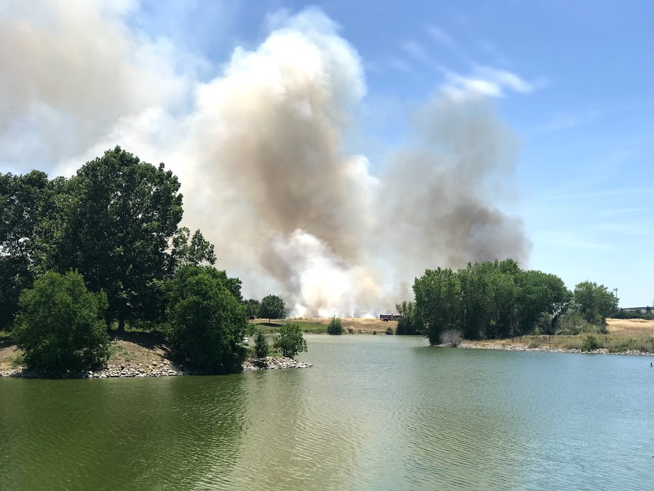 Image of lake in foreground and large billow of brown smoke in background.