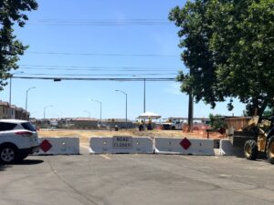 Image of road with three cement blockades and "Road Closed" sign in foreground. In background road crews consulting.