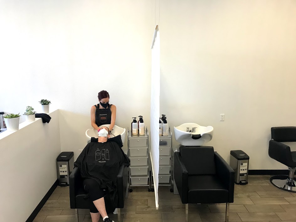 Image of two shampoo bowls separated by a partition. One bowl has a stylist shampooing a customer's hair.