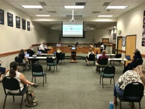 Image of board meeting room where chairs and people are spread out.