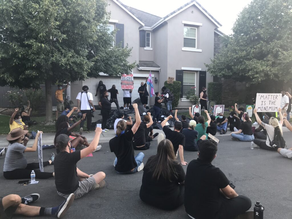 Image of protesters seated on road with arms raised.