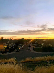 Image of neighborhood street with sunset in the distance. Appears to be taken from a higher elevation.