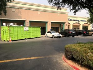 Image of building with large dumpster blocking part of the front. The Kids Care Dental sign can be seen in the background.