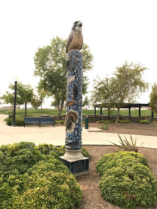 Image of pillar sculpture with hawk on top. Different species of birds are sculpted on the pillar.