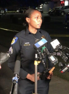 Image of police officer standing in front of several TV microphones.