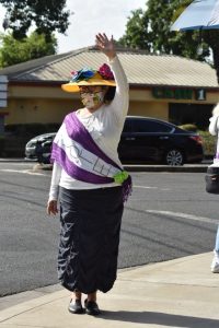 Image of woman dressed as a suffragist from the early 1900s wearing a purple sash with the word "vote" written on it.