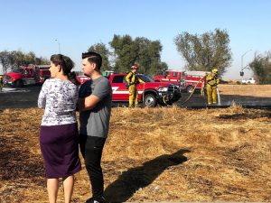 Image of woman and man watching firefighters mop of grass fire.