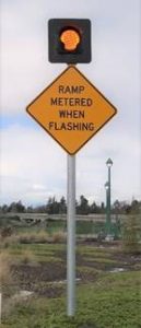 Image of yellow caution sign which with a light mounted on top. It reads "ramp metered when flashing."