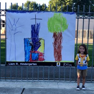 Image of small boy standing next to banner inspired by his drawing.