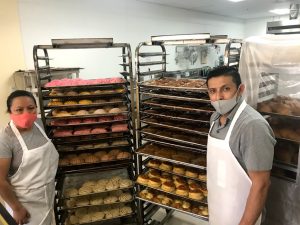 Image of woman and man standing next to stacked trays of Mexican pastries.