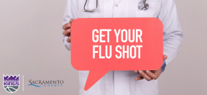 Image of person in white lab coat, wearing stethoscope around their neck and holding a sign which reads "get your flu shot."