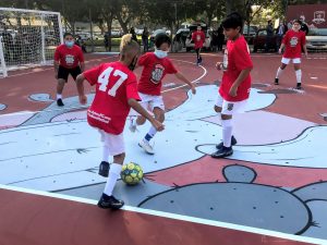 Image of three boys vying for soccer ball on hard futsal court.