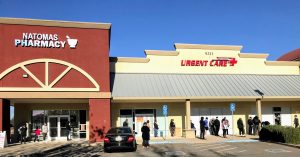 Image of line of people standing in front of a building which reads Natomas Pharmacy and Natomas Urgent Care.