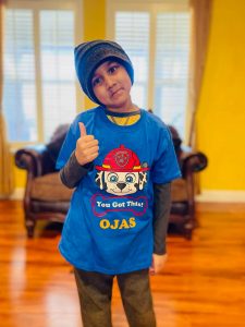 Image of boy wearing beanie on his head giving a thumbs up. He's wearing a t-shirt which reads "You Got This! Ojas"