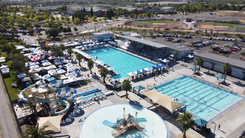 Aerial image looking down on the aquatics complex where tents surround the pools, swimmers compete and spectators sit in the stands.