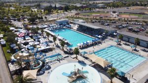 Ariel image looking down on the aquatics complex where tents surround the pools, swimmers compete and spectators sit in the stands.