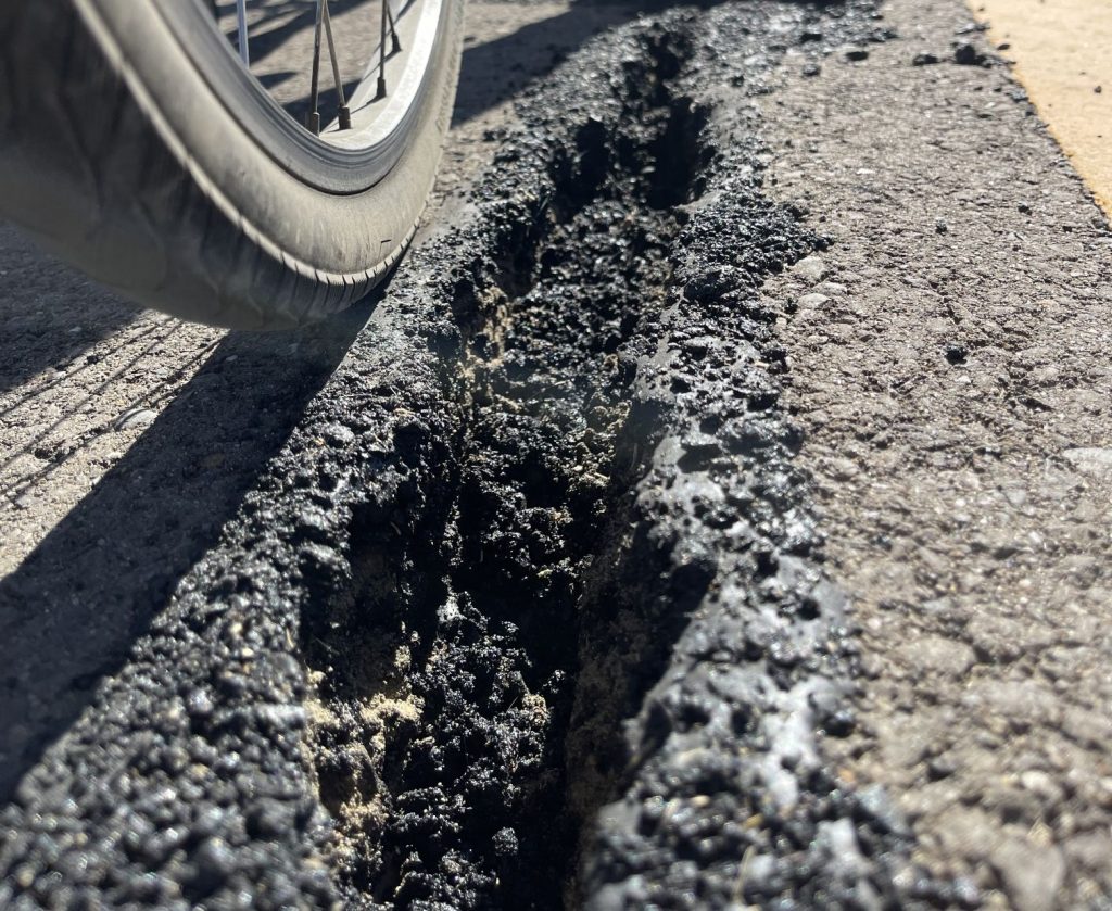 Image of a wide crack in the asphalt trail. Next to it is a bicycle tire to provide perspective.