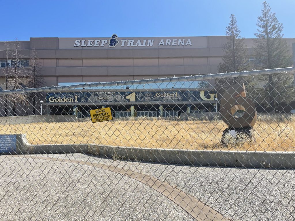 Image of large concrete building in background and a cyclone fence in foreground. The iconic 6th Man Statue is visible behind the fence. The words Sleep Train Arena are on the building.
