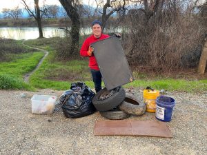 Image of a teenage boy wearing a red sweatshirt who is surrounded by garbage and debris collected along the river.