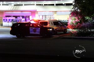 Image of a lighted gas station at night. There are several police cars and yellow crime tape surrounding the area.