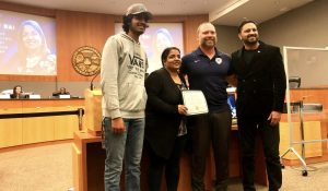 Image of a woman holding a certificate, one man is standing on her left and two to her right.