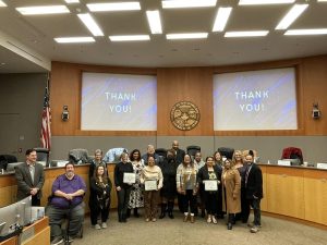 Image of large group of individuals who received awards. They are joined by the commissioners. Two large screens read Thank You.